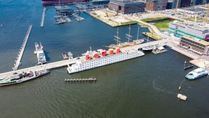 A large cruise ship docked at a port with a pier extending into the water. - Botel (Amsterdam)
