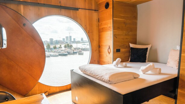 A modern room with a circular window, a bed with white linens, and a wooden interior. - Botel (Amsterdam)