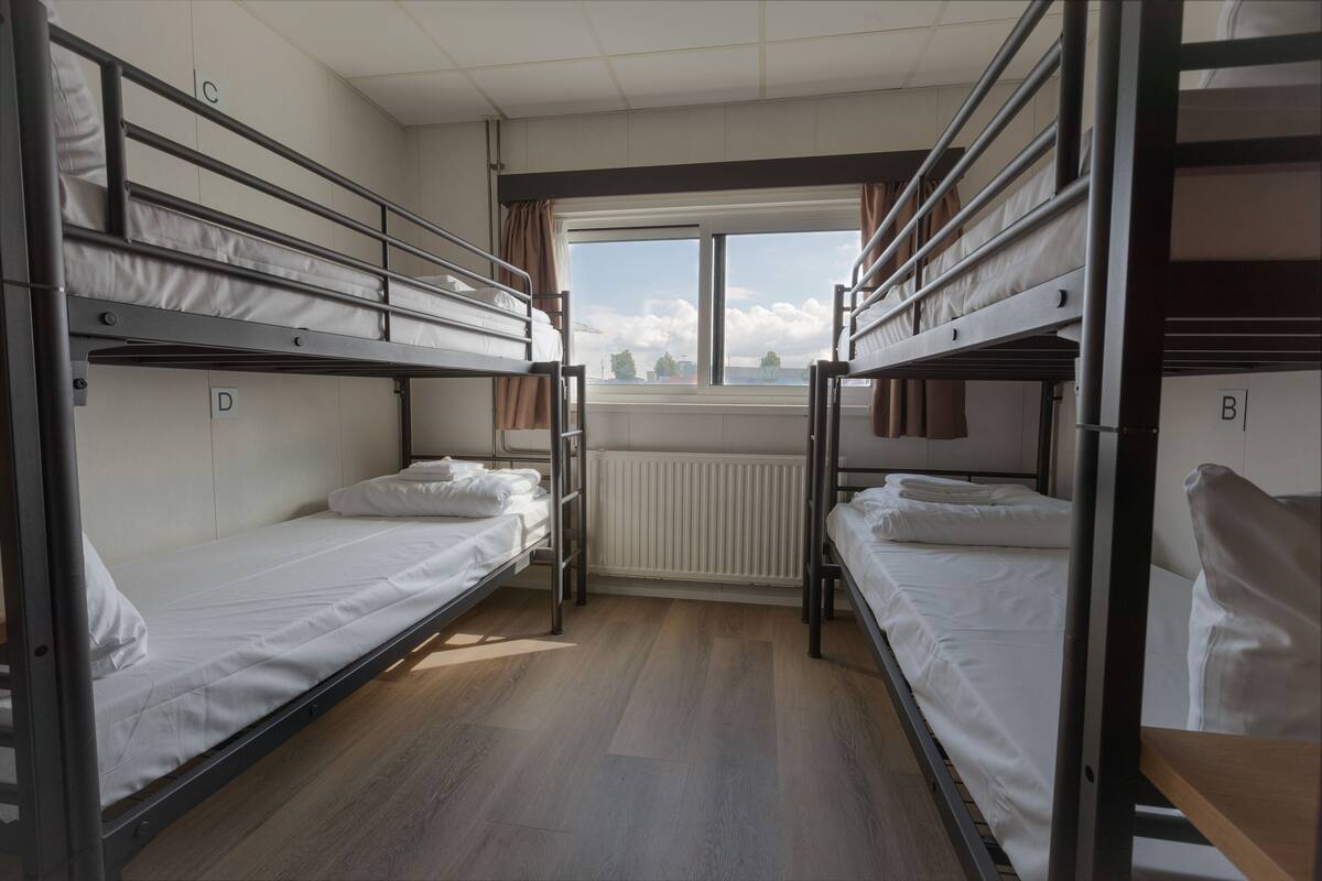 Une chambre de dortoir avec des lits superposés, une fenêtre donnant sur un paysage agréable et un radiateur.