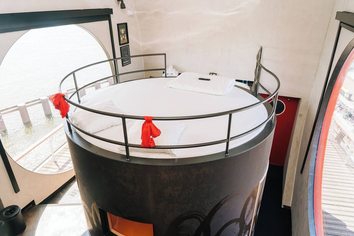 Un lit rond avec une barrière en métal, un matelas blanc et une serviette rouge.
