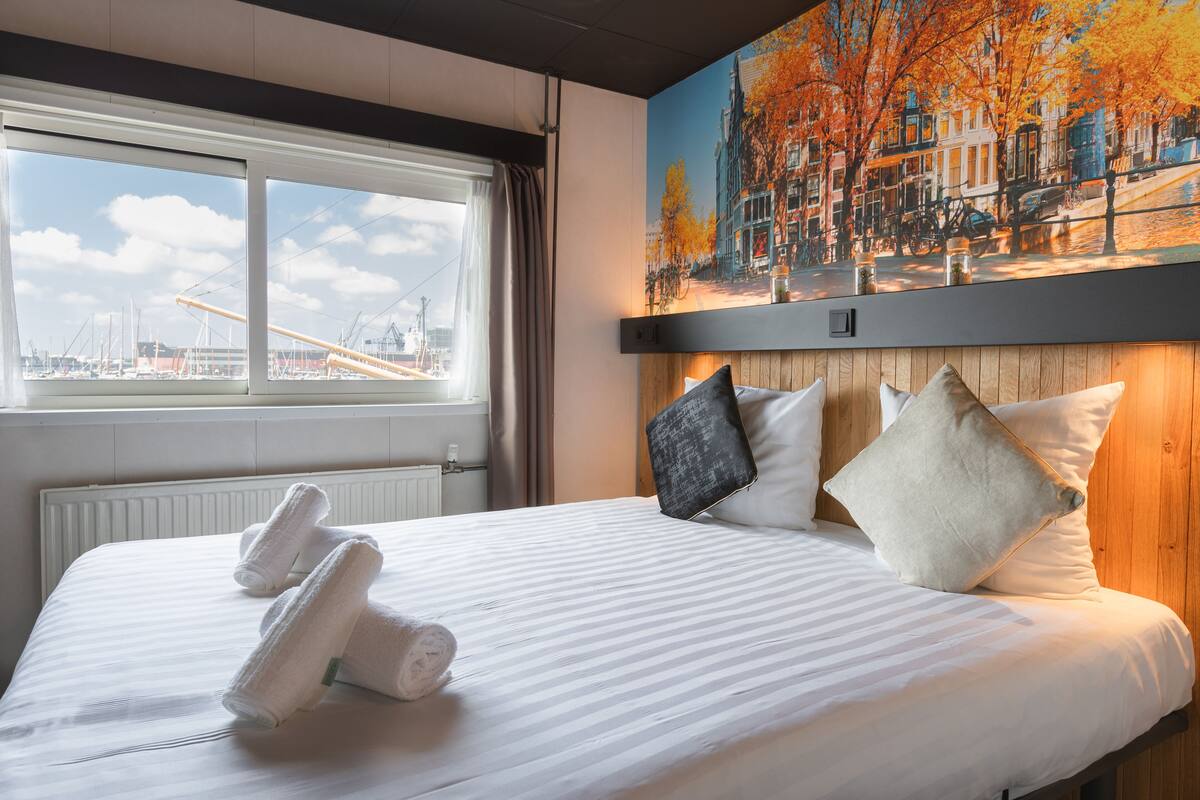 Une chambre d’hôtel avec un grand lit, une fenêtre donnant sur un paysage urbain et un tableau au-dessus du lit.