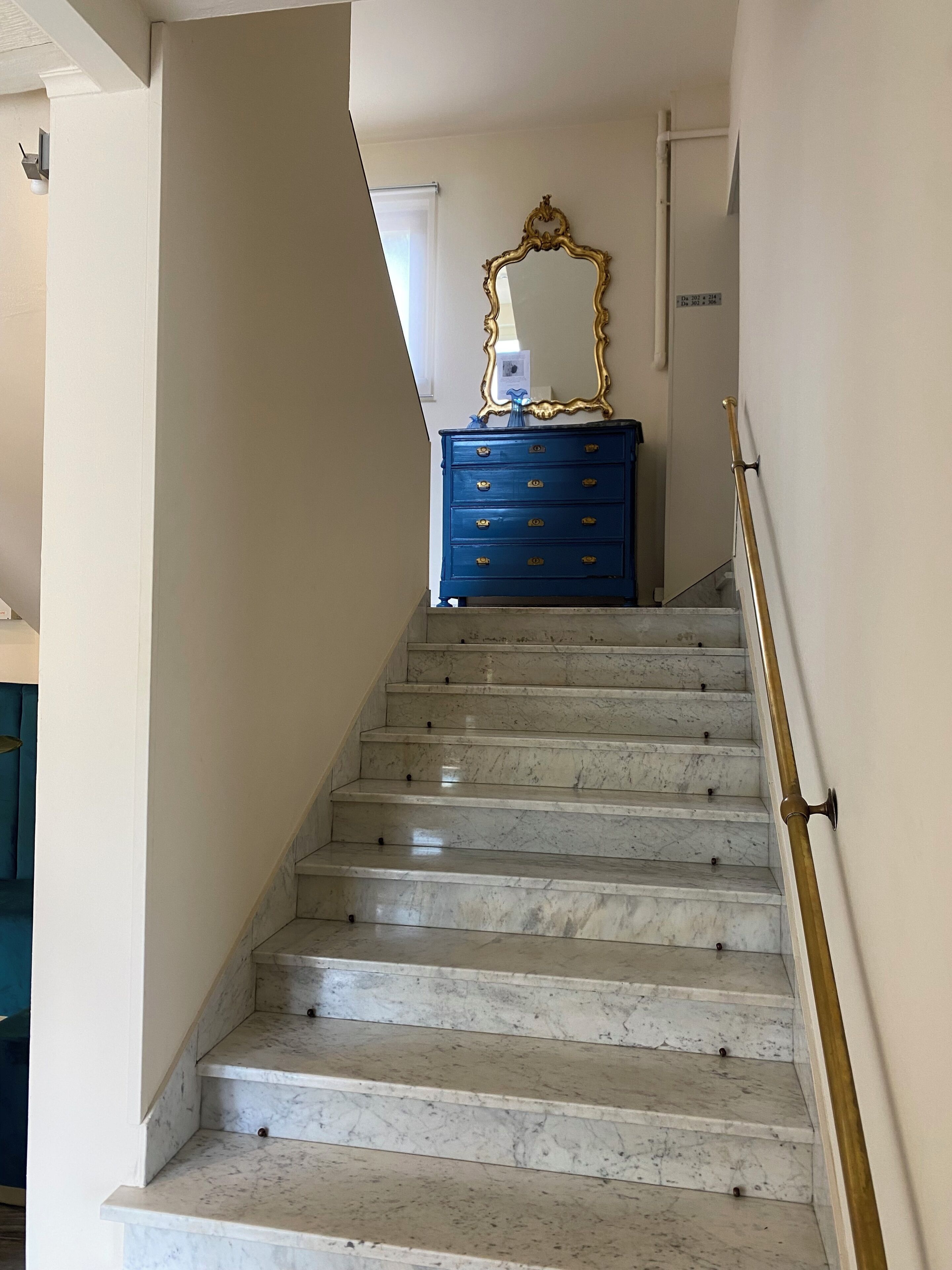A marble staircase with a blue dresser and a gold-framed mirror at the top.