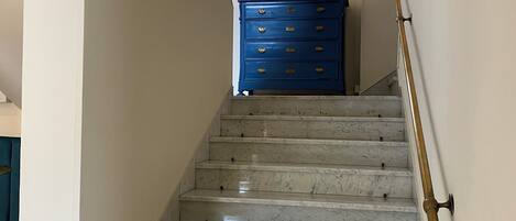 A marble staircase with a blue dresser and a gold-framed mirror at the top.