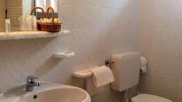 Un baño con lavamanos, inodoro, bidé y un estante con artículos de tocador.
