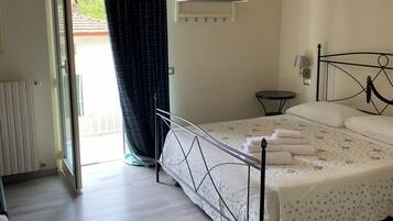 A bedroom with a bed, a bedside table, a hanging light fixture, a window with curtains, and a view of the outside.