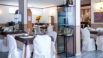 Een restaurant met meerdere tafels klaar voor diners, elk met witte stoelen en een glazen vitrine in het midden.