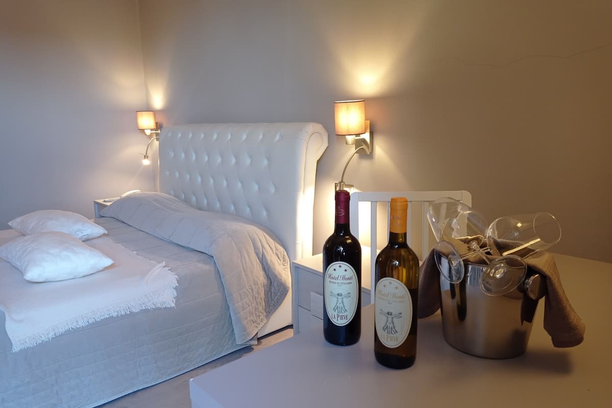 A bed with a white headboard, two wall-mounted lamps, and two bottles of wine on a bedside table.