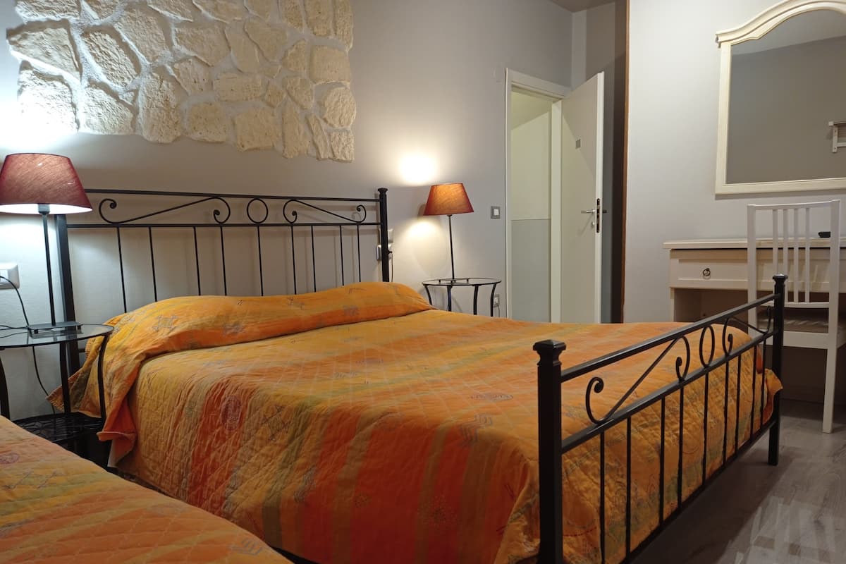 A bedroom with two beds, a stone wall, a mirror, and a dresser.