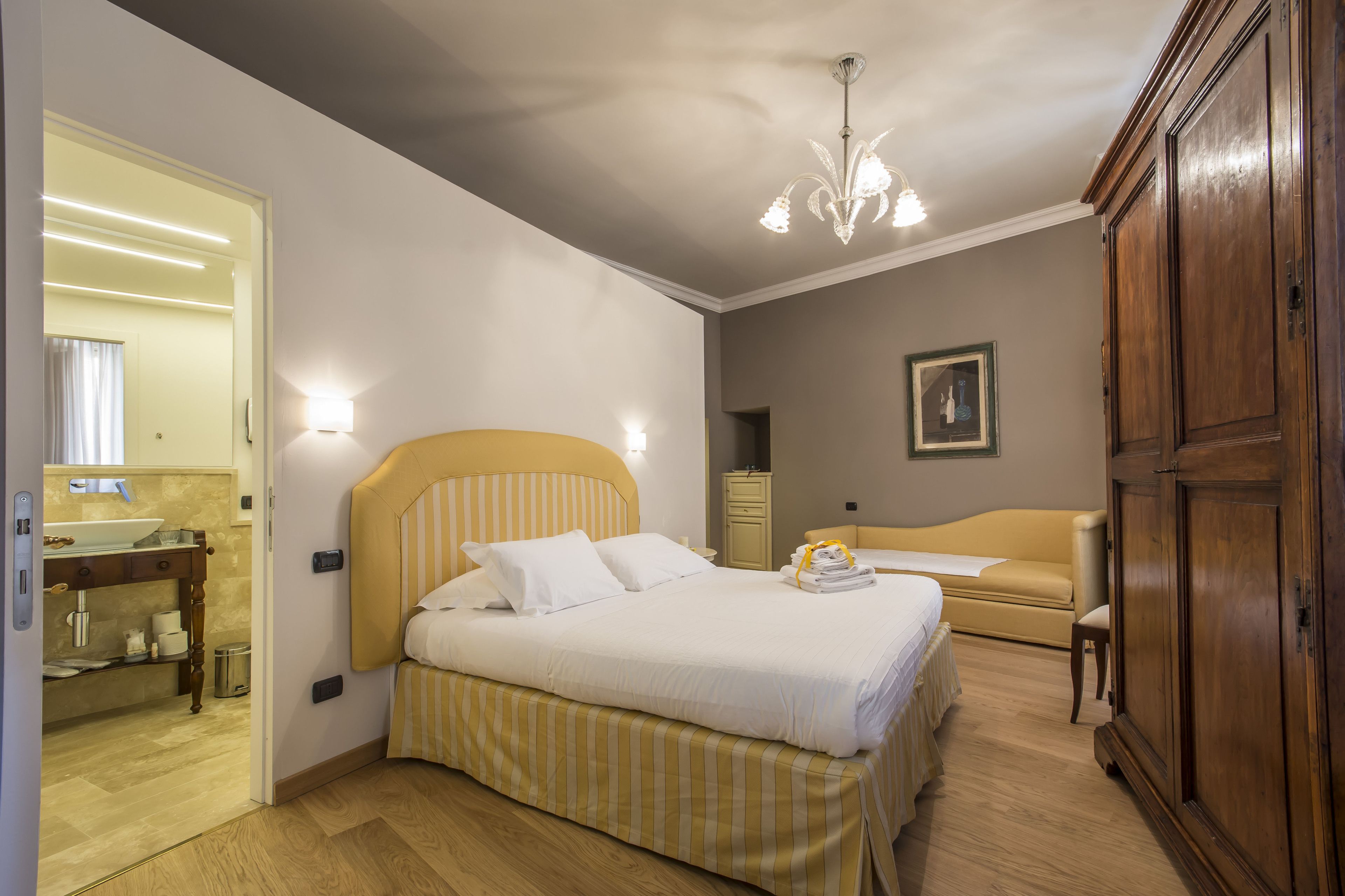 A hotel room with a bed, bedside table, wardrobe, and a bathroom visible through an open door.