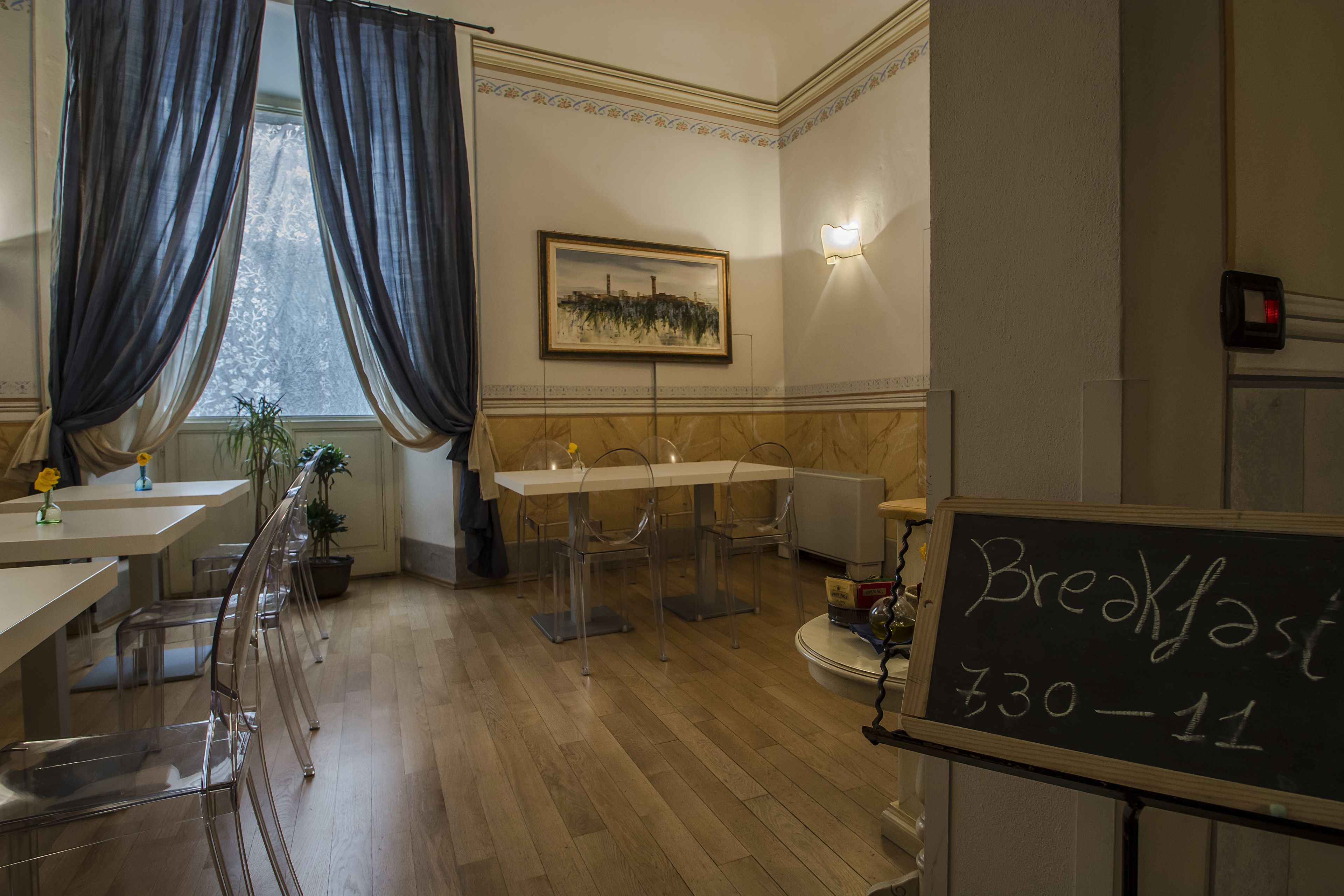 A breakfast area with a chalkboard menu, clear chairs, and a table with a vase of flowers.
