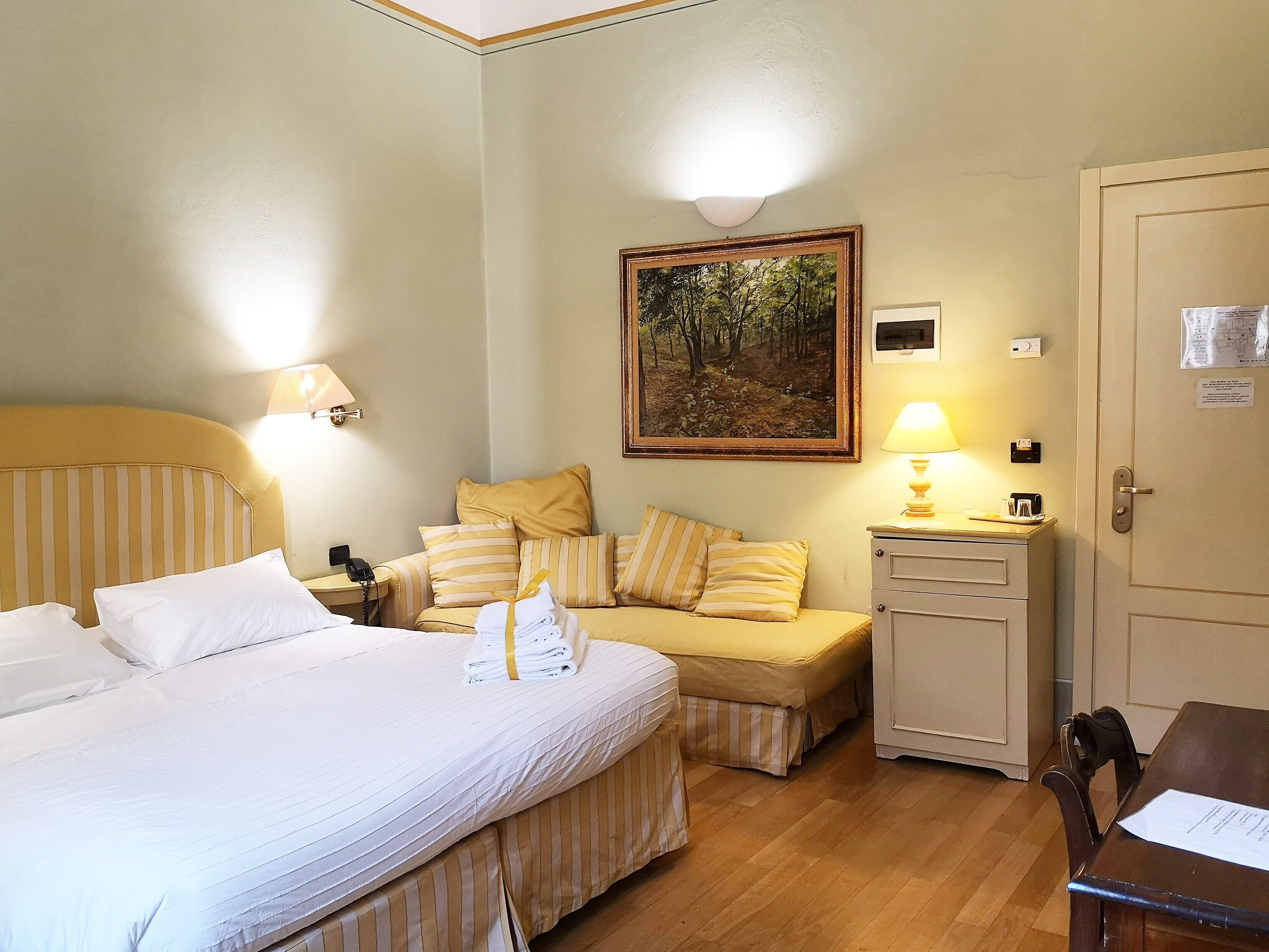 A hotel room with a bed, a sofa, a desk, and a door.