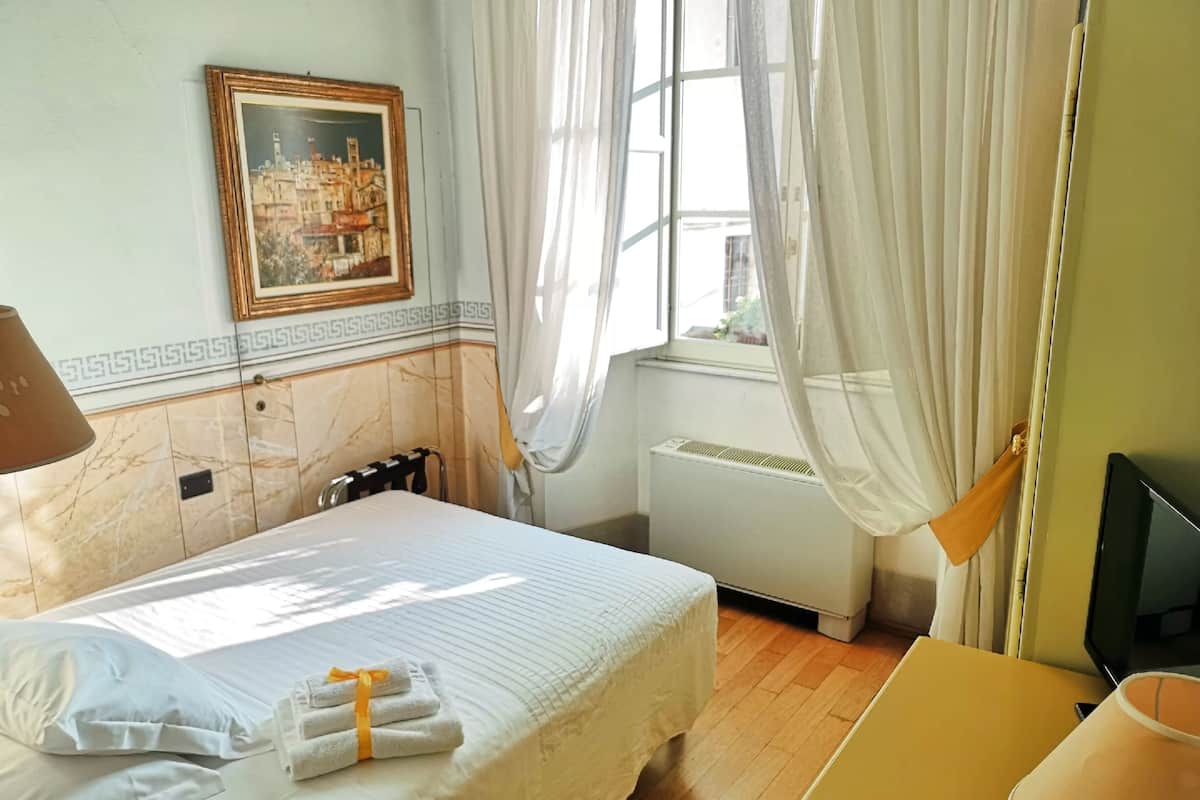 Habitación de hotel con cama, escritorio, televisión y ventana con cortinas.