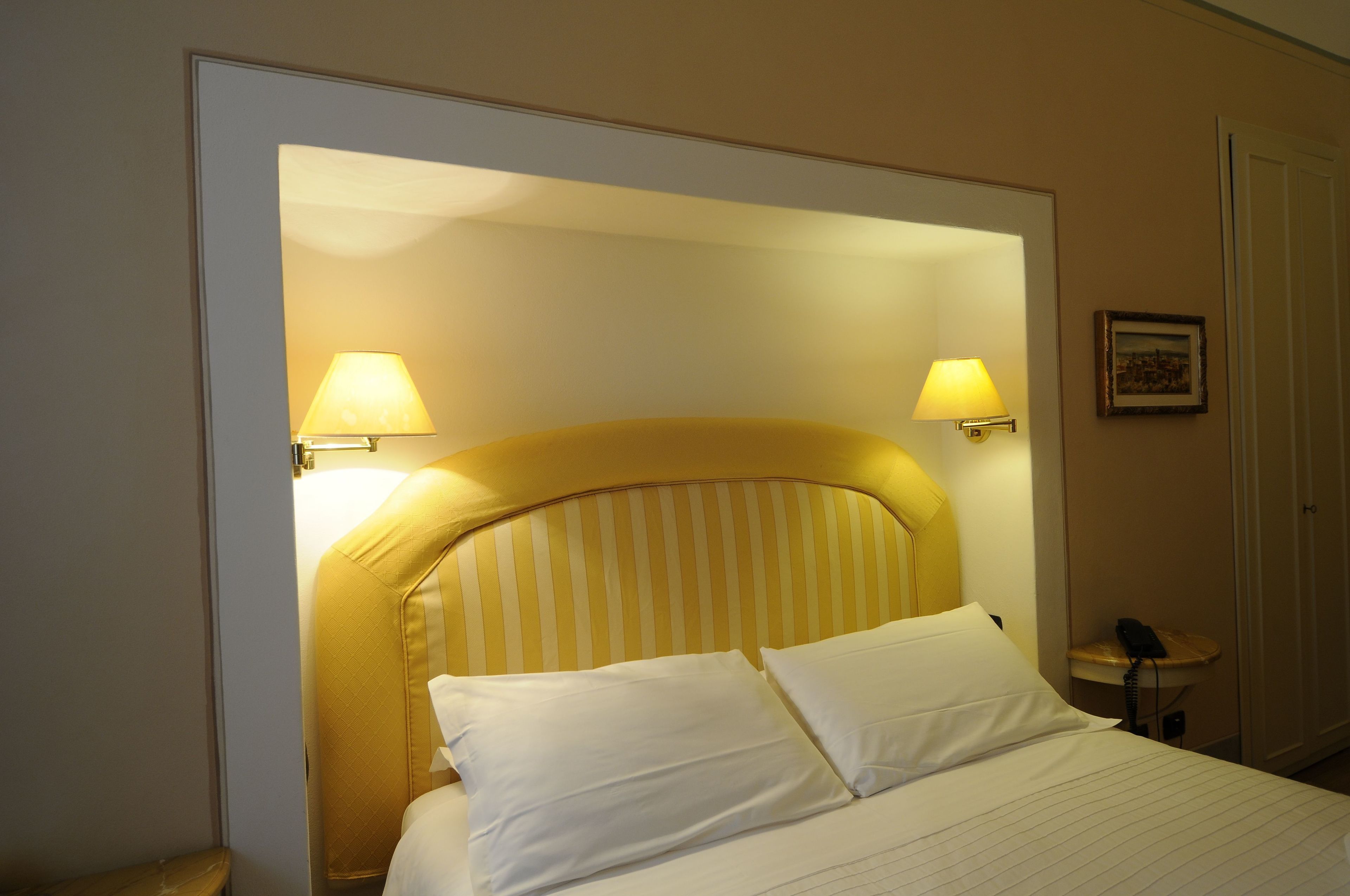 A hotel room with a bed, two bedside lamps, a telephone, and a framed picture on the wall.