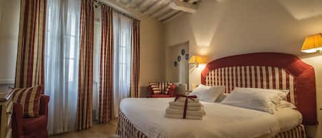 A hotel room with a large bed, striped curtains, a red chair, and a lamp.