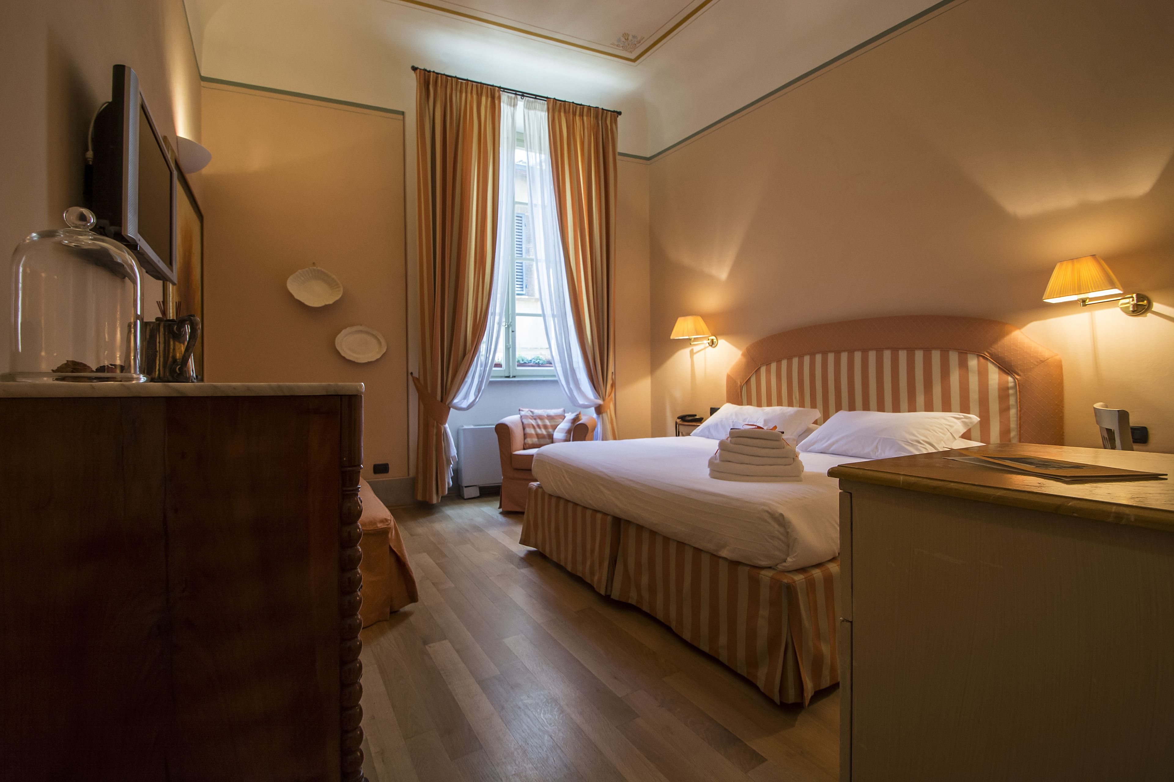 Ett hotellrum med en säng i trä, ett skrivbord, en lampa och ett fönster med gardiner.