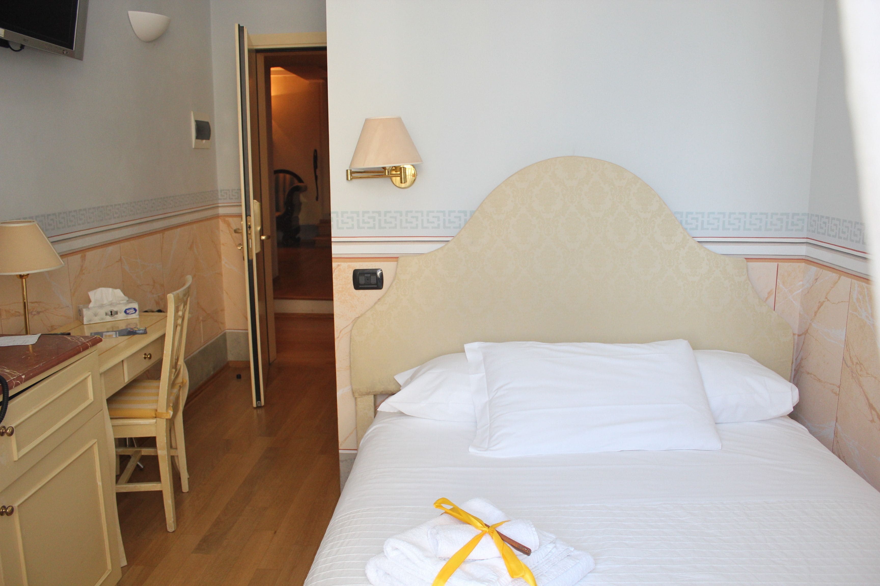 A hotel room with a bed, a desk, a chair, and a TV mounted on the wall.