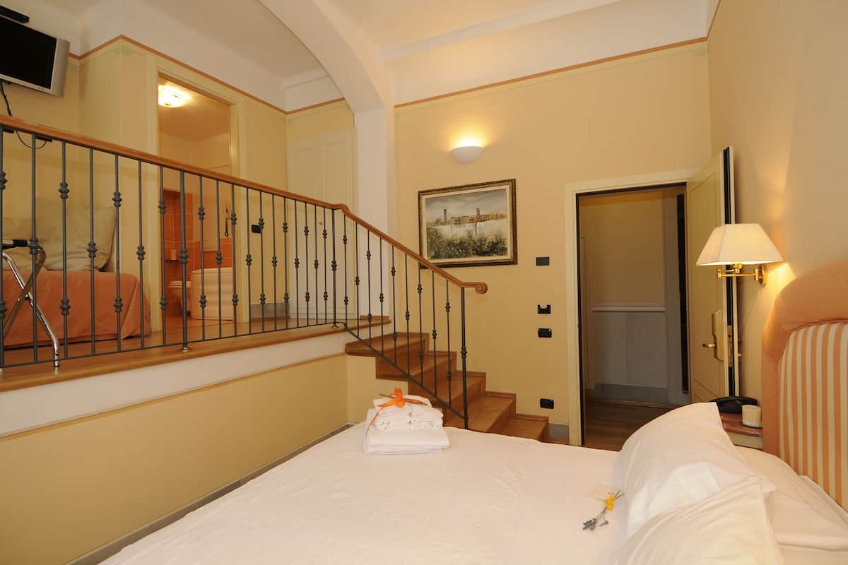 Habitación de hotel con cama, una escalera de madera, un cuadro en la pared y una lámpara.