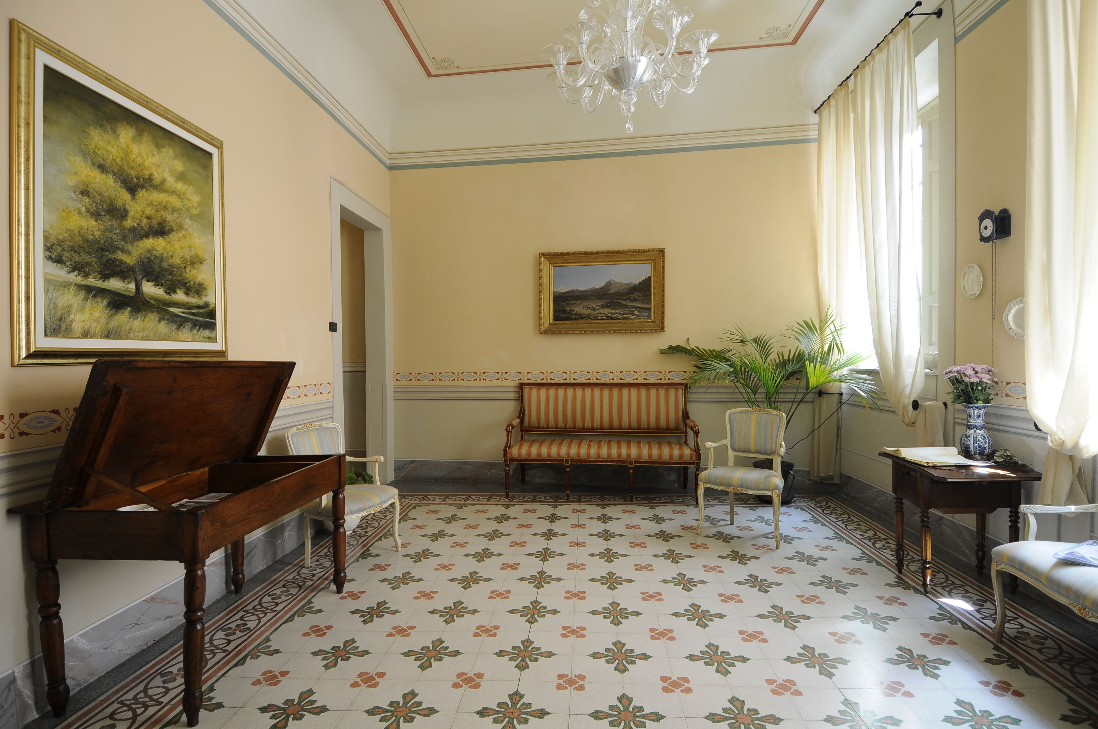 Ein Zimmer mit einem Klavier, einem Sofa, einem Sessel, einem Tisch mit einer Vase und einem Bild an der Wand.