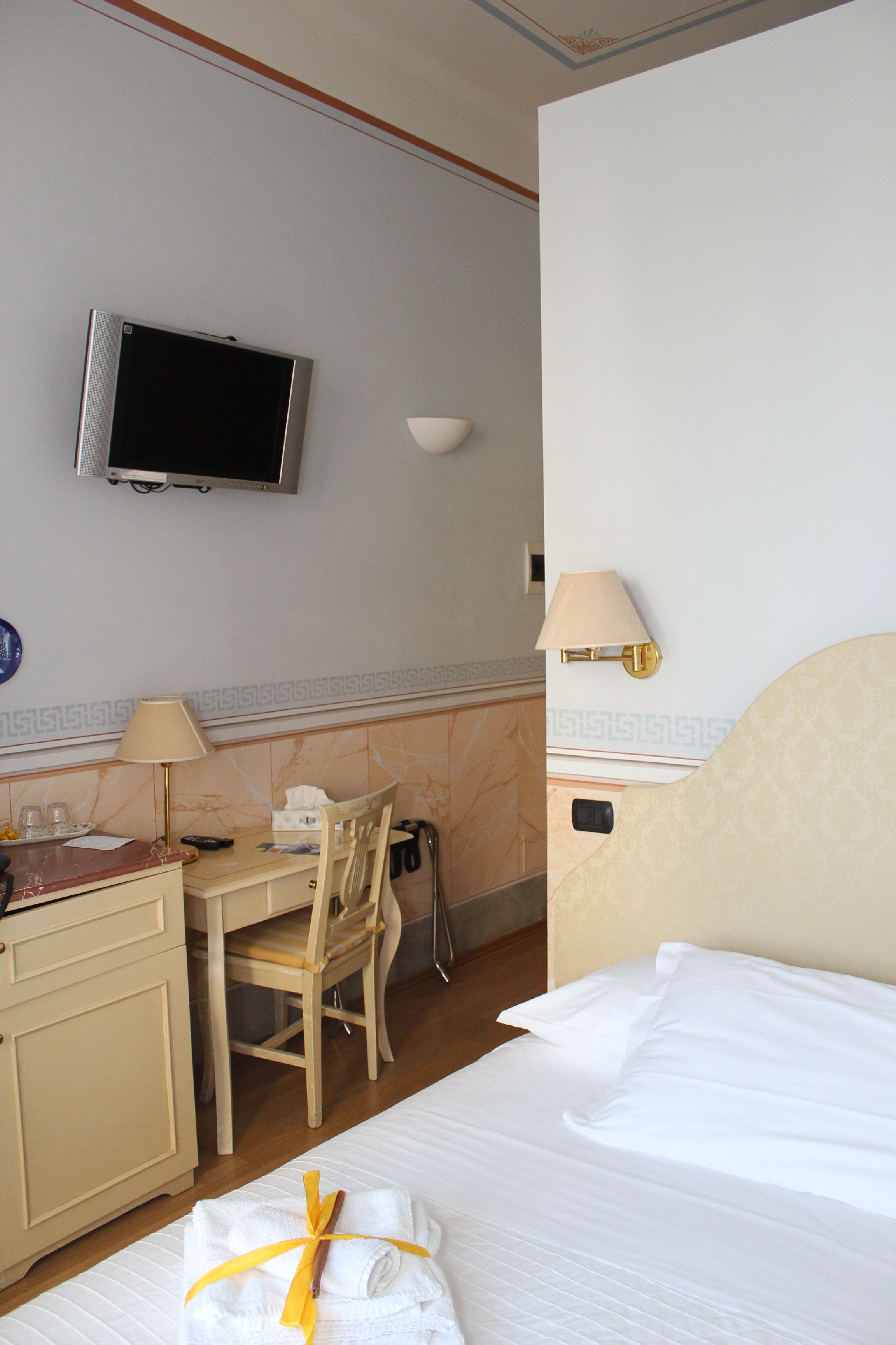 A hotel room with a bed, a desk with a chair, a television, and a lamp.