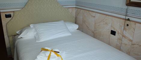 A neatly made bed with white linens and a yellow towel, a headboard with a decorative pattern, and a wall-mounted lamp.