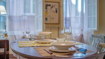 Una mesa de comedor con platos, tazones, vasos y cubiertos, con una ventana y cortinas al fondo.