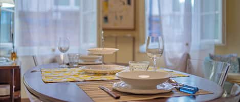 A dining table set with plates, bowls, glasses, and cutlery, with a window and curtains in the background.