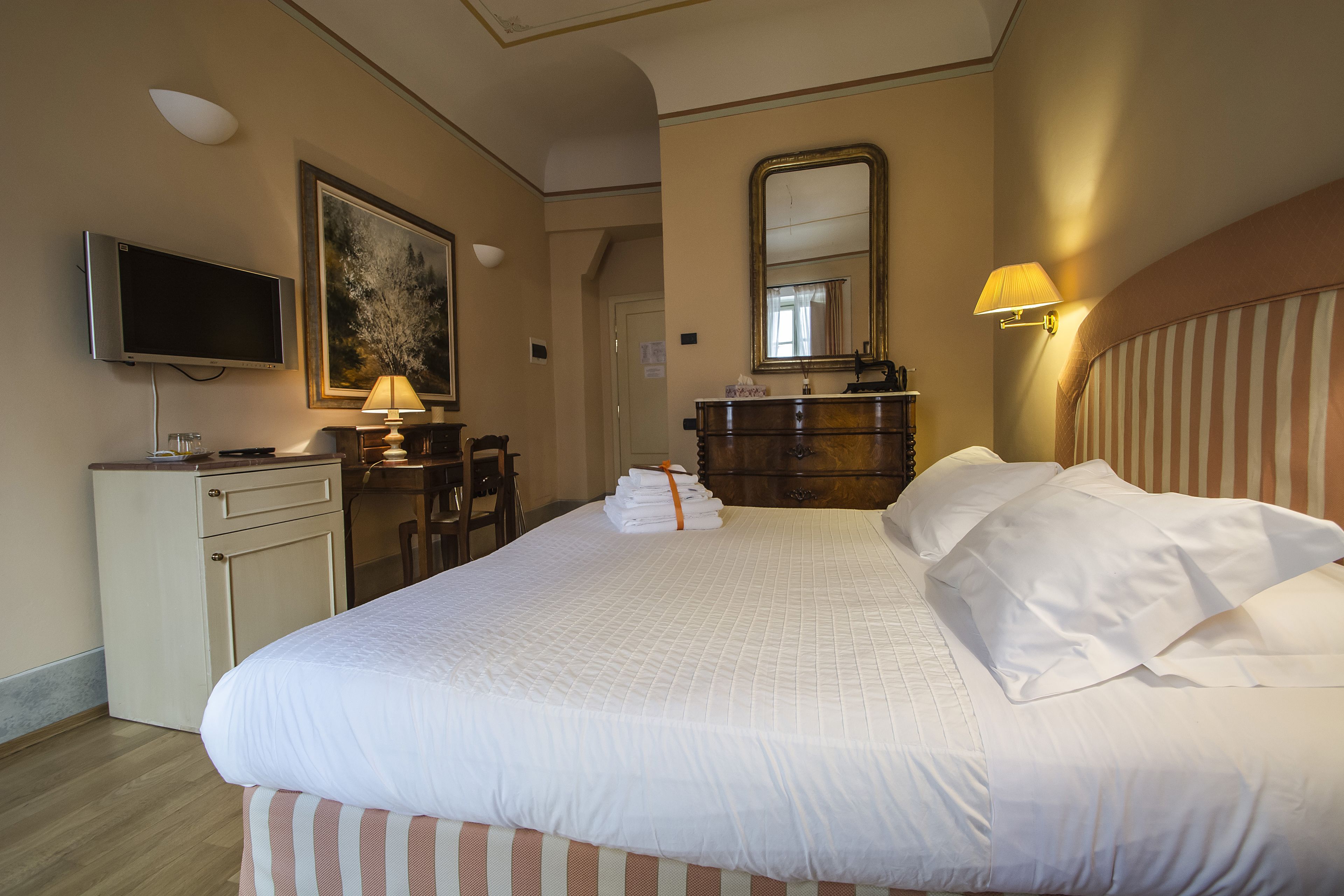 Une chambre d’hôtel avec un grand lit, un téléviseur posé sur un meuble, un bureau et un miroir au mur.
