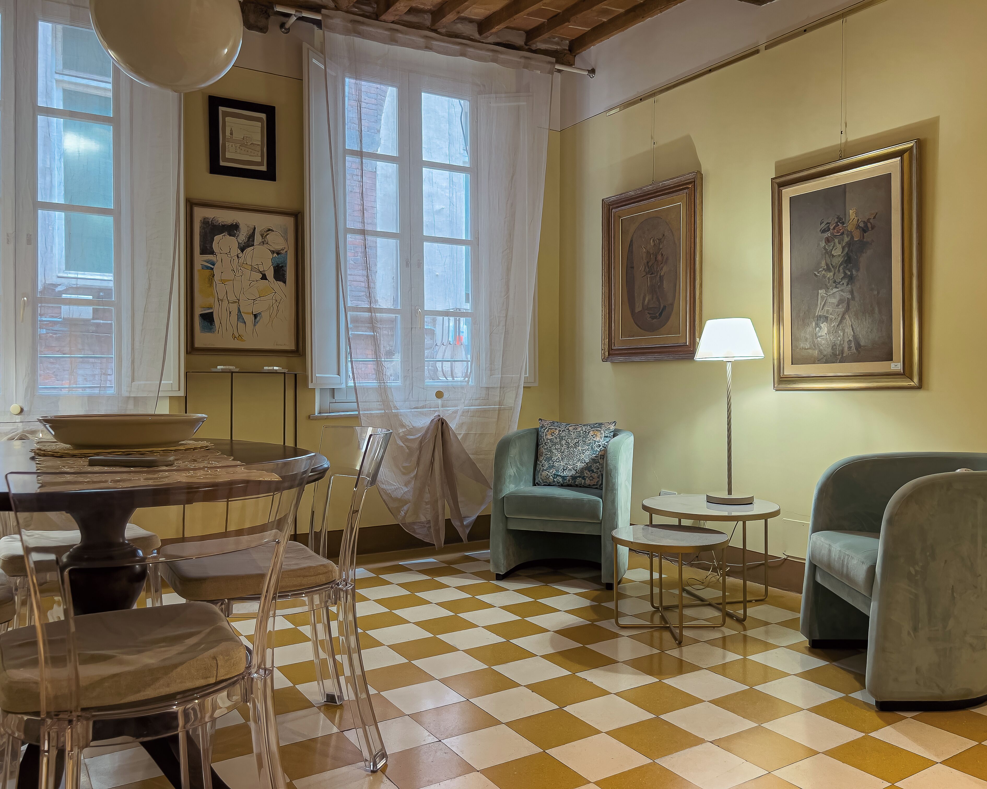 A living room with a checkered floor, a dining table, chairs, a sofa, a lamp, and artwork on the walls.