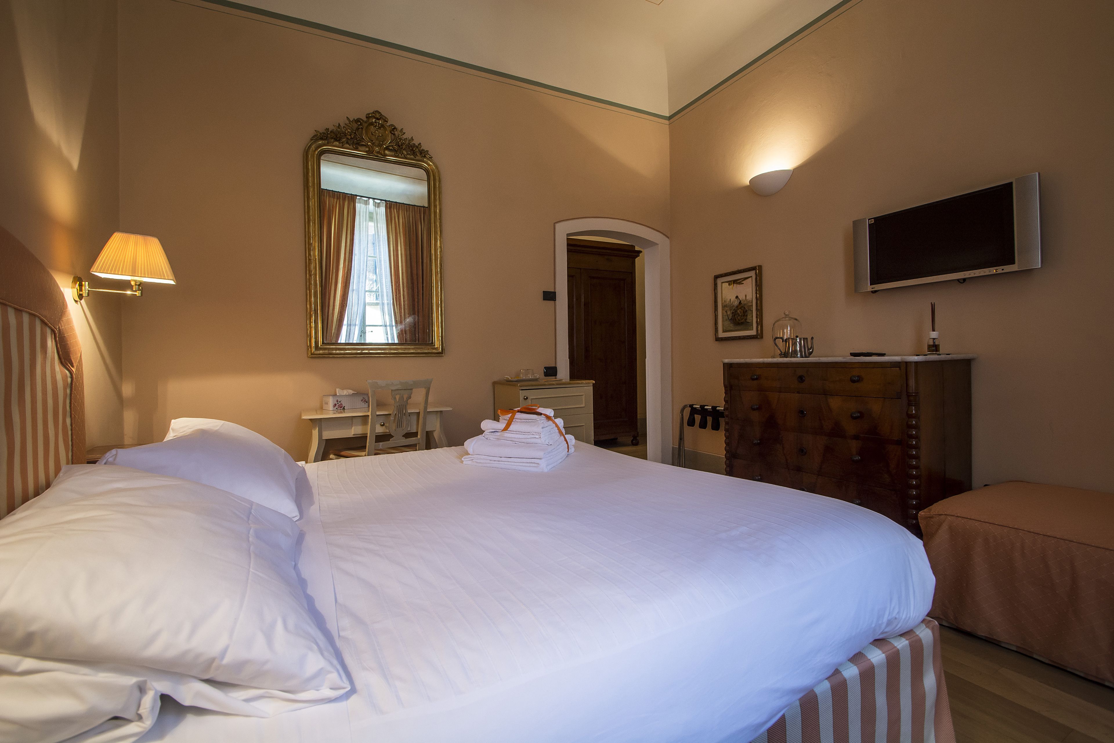 A hotel room with a large bed, a desk, a dresser, a television, and a mirror.