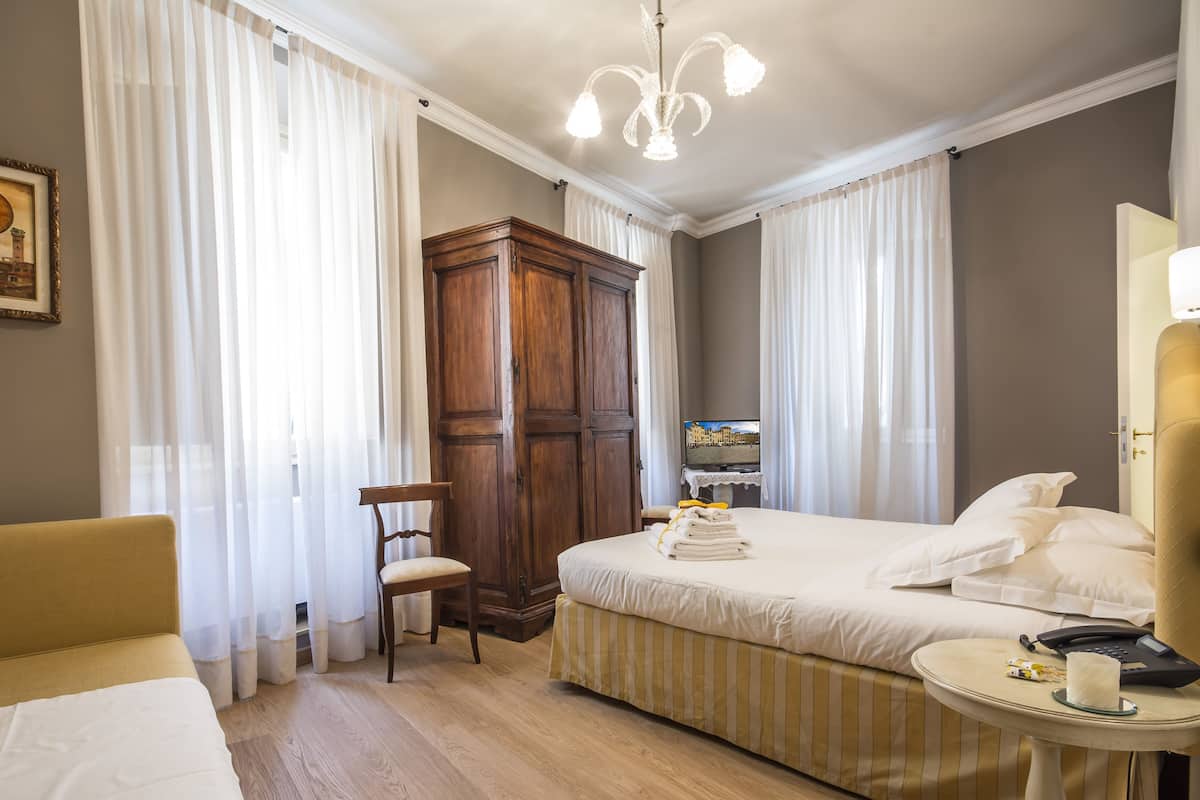 Habitación de hotel con cama, una silla, armario, mesita de noche con teléfono y un cuadro en la pared.