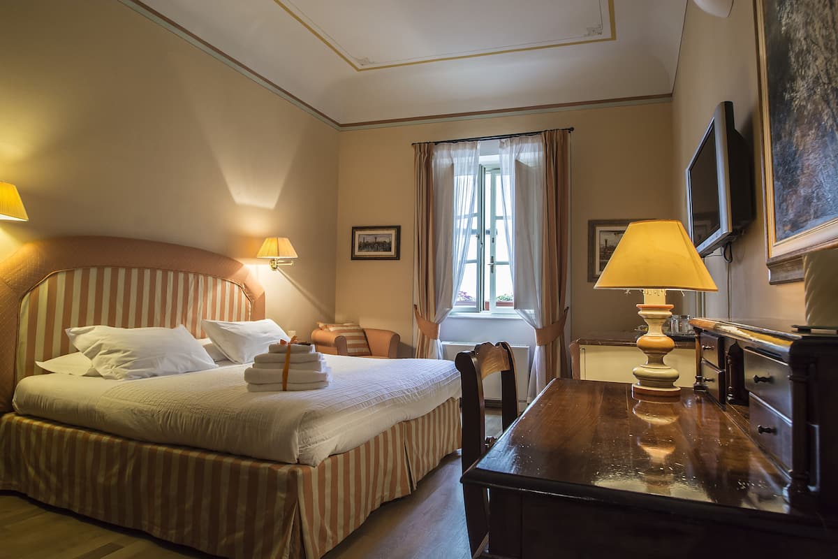 Habitación de hotel con cama, escritorio, silla, televisor y ventana con cortinas.