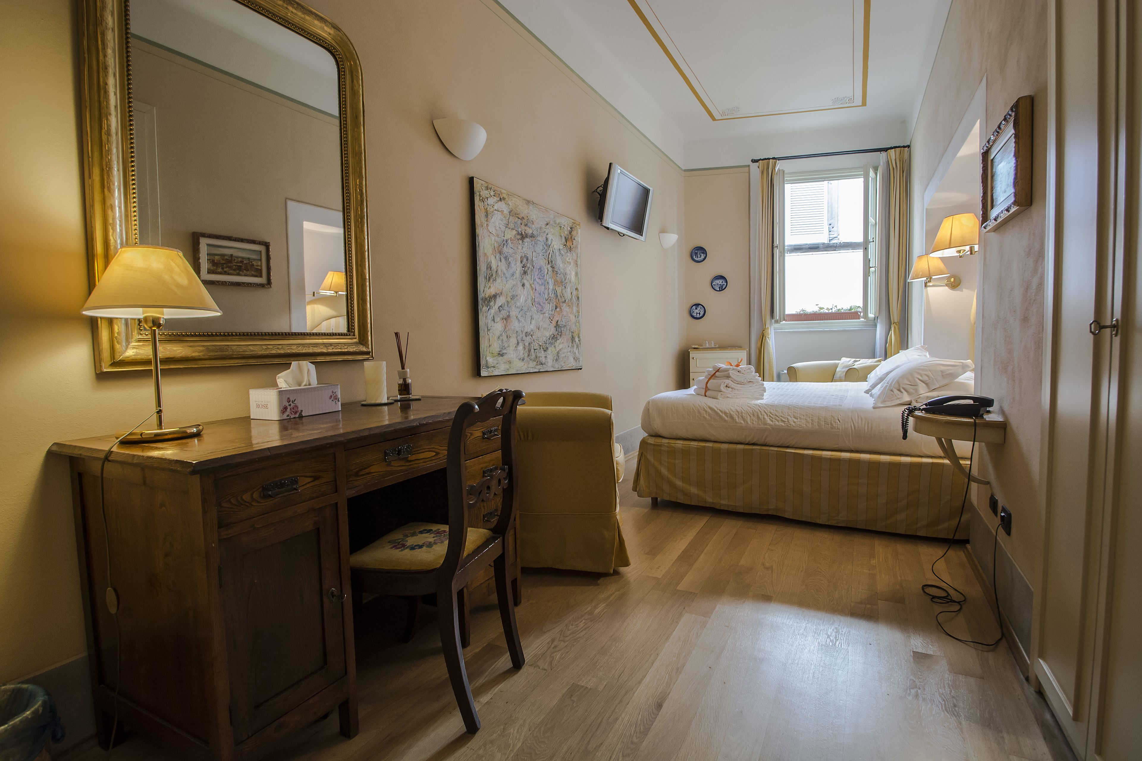 Une chambre d’hôtel avec un bureau en bois, une chaise, un lit, une télévision et une fenêtre avec des rideaux.