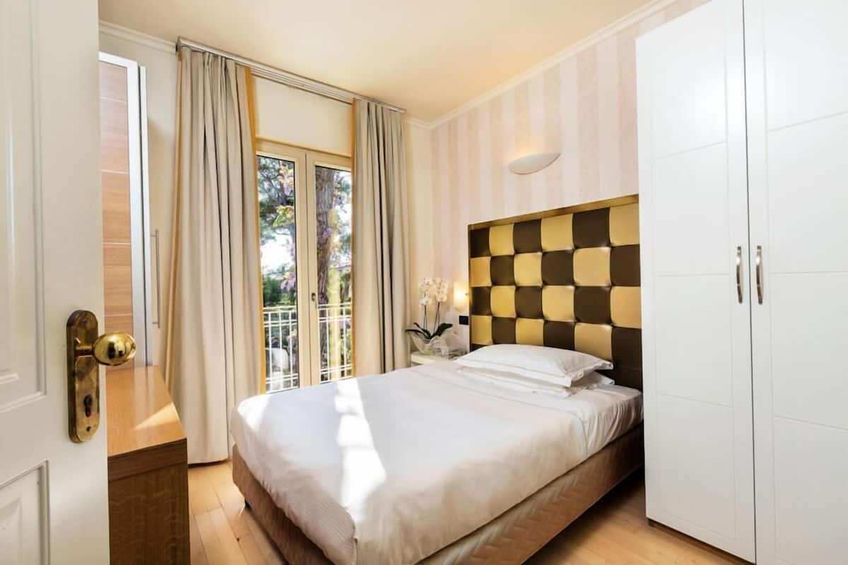 Een slaapkamer met een bed, een kledingkast, een deur met een handgreep en een raam met gordijnen.