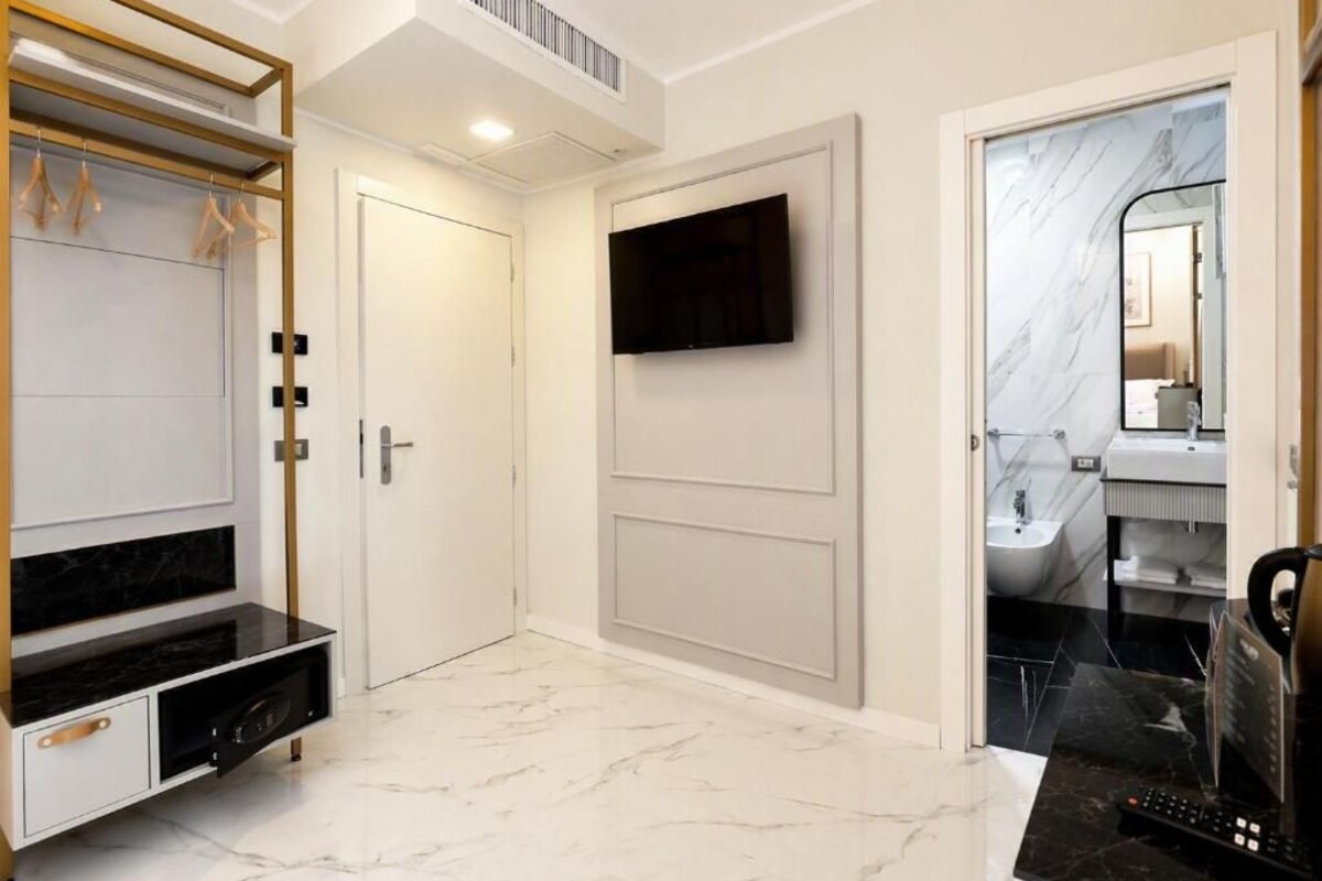 Une chambre d’hôtel dotée d’un téléviseur à écran plat fixé au mur, d’un meuble de rangement intégré pour les équipements multimédias, d’une salle de bain avec un lavabo et un miroir, et d’un sol en marbre.