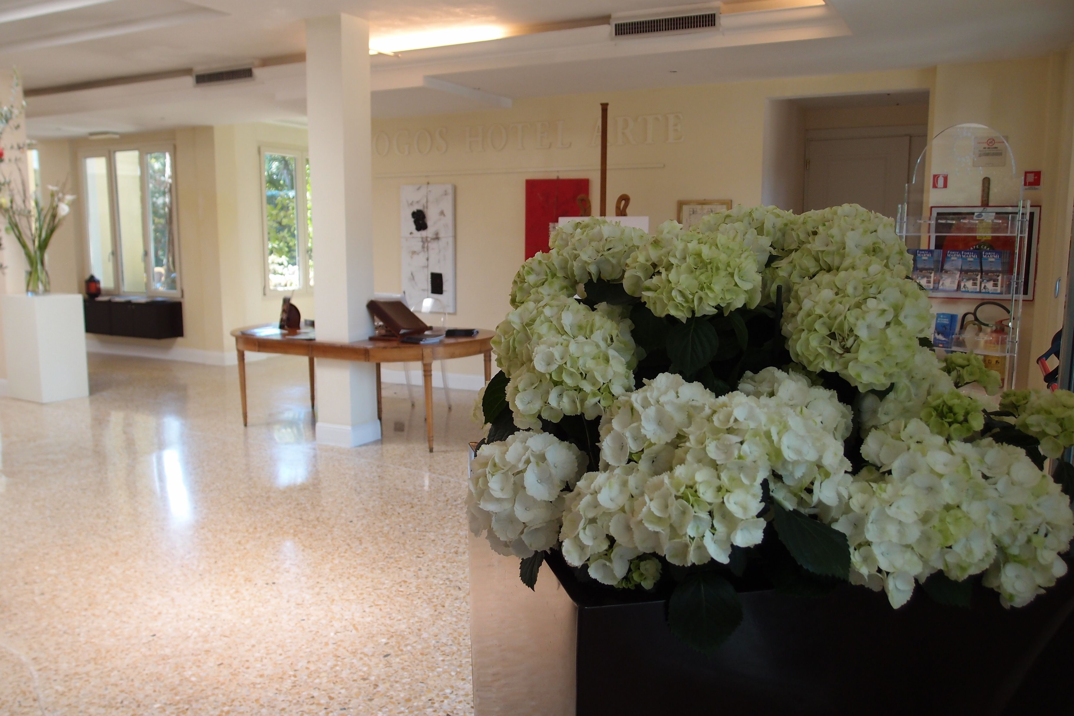 A lobby with a reception desk, a large vase of white flowers, and a wall with the hotel name.