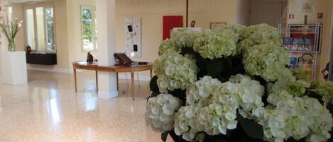 A lobby with a reception desk, a large vase of white flowers, and a wall with the hotel name.