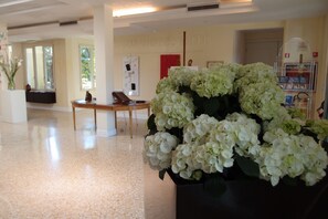 Un hall d’entrée avec un comptoir de réception, un grand vase rempli de fleurs blanches et un mur sur lequel est inscrit le nom de l’hôtel.
