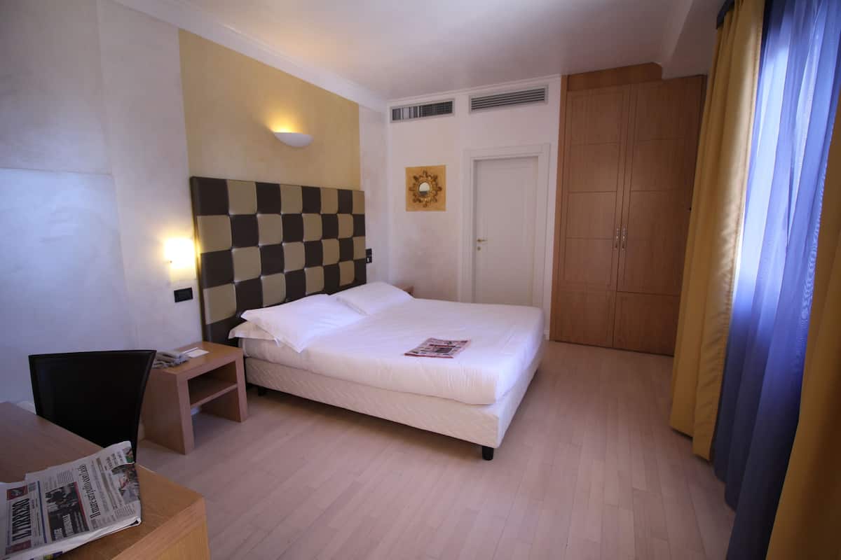 Een hotelkamer met een bed, nachtkastje, stoel en een klein bureau met een krant.