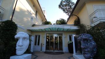 Entrada do Hotel Logos, com porta de vidro, um busto de mármore à esquerda e uma grande escultura à direita.