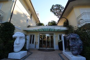 La entrada del Hotel Logos con una puerta de cristal, un busto de mármol a la izquierda y una escultura grande a la derecha.