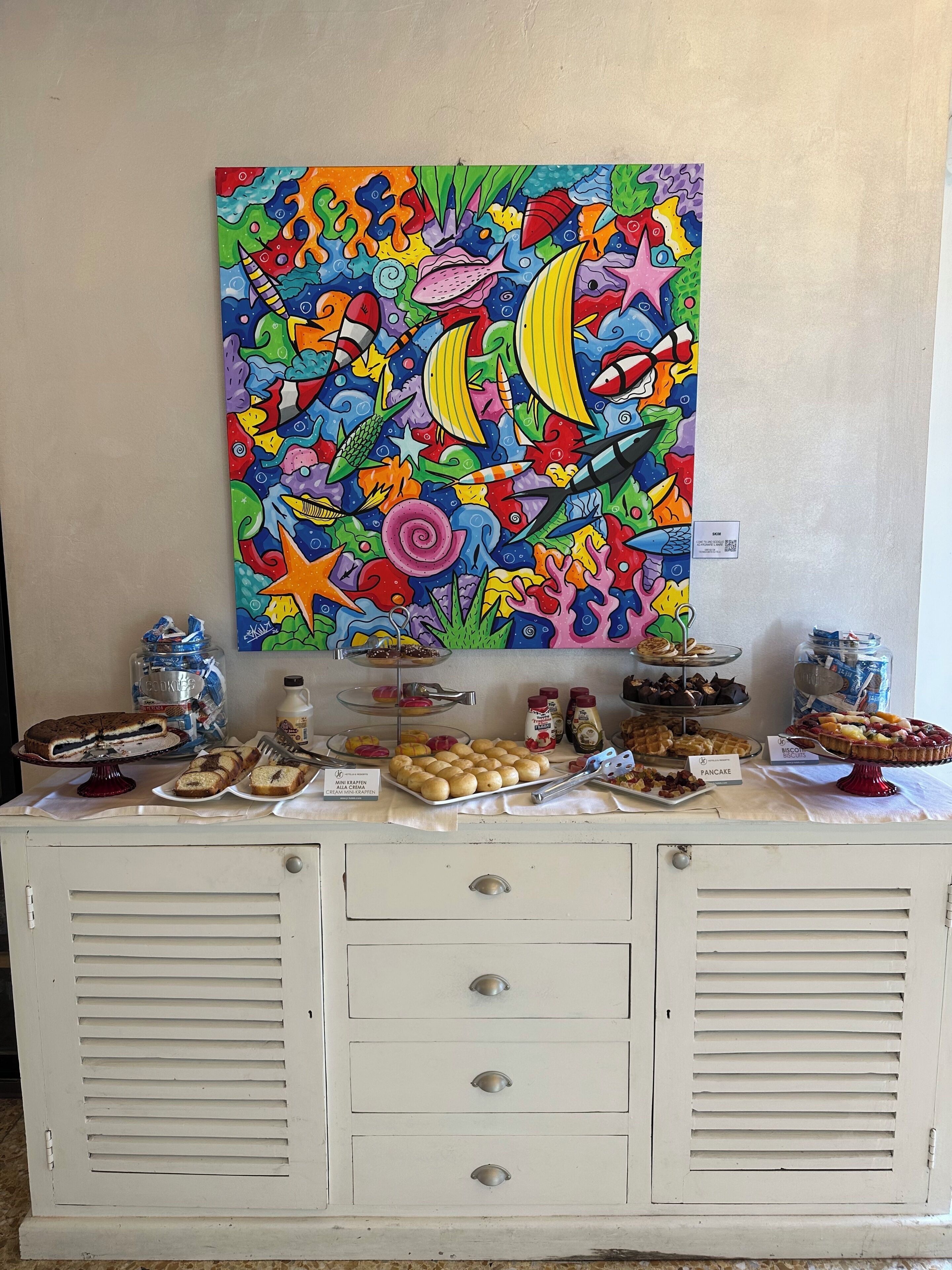 A buffet table with various food items and a colorful painting above it.