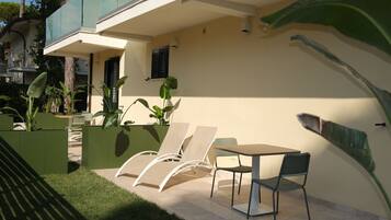 Um pátio externo com mesa e cadeiras, rodeado por vegetação e um edifício.