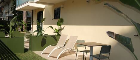 Une terrasse extérieure avec une table et des chaises, entourée de verdure et bordée d’un bâtiment.