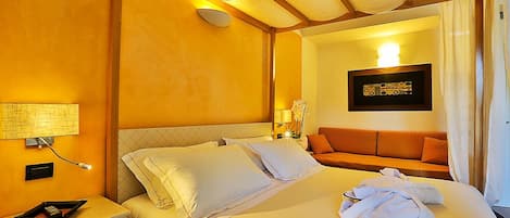 Quarto de hotel com cama, mesa de cabeceira, luminária, quadro pendurado na parede e janela com cortinas.