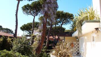 A garden with trees, a white fence, and a building with a tiled roof.