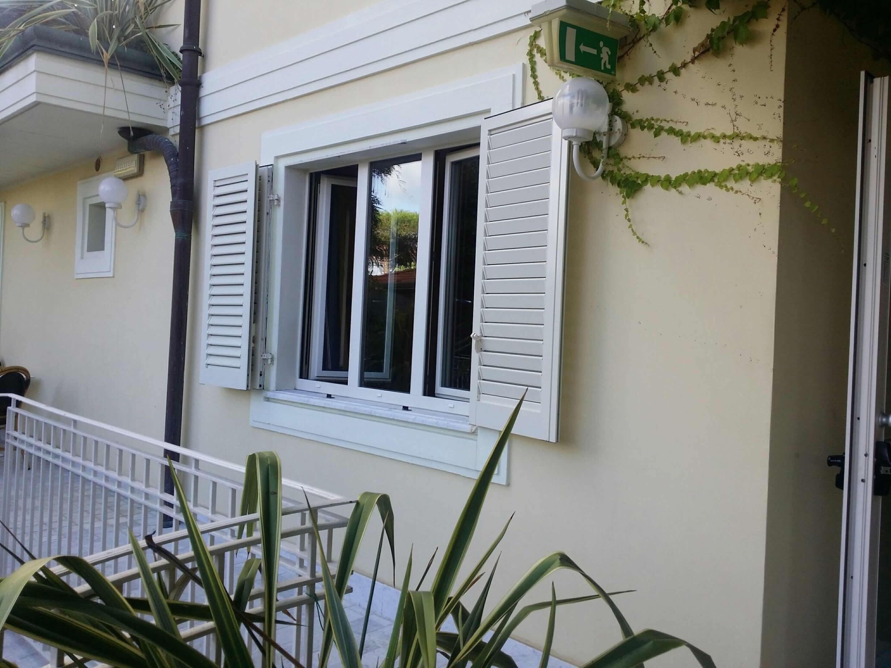 A building with a window with white shutters, a green exit sign, and a white railing.
