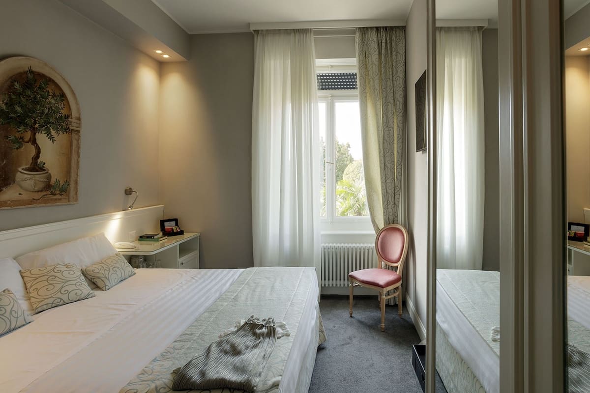 A hotel room with a large bed, a chair, a desk, and a window with curtains.
