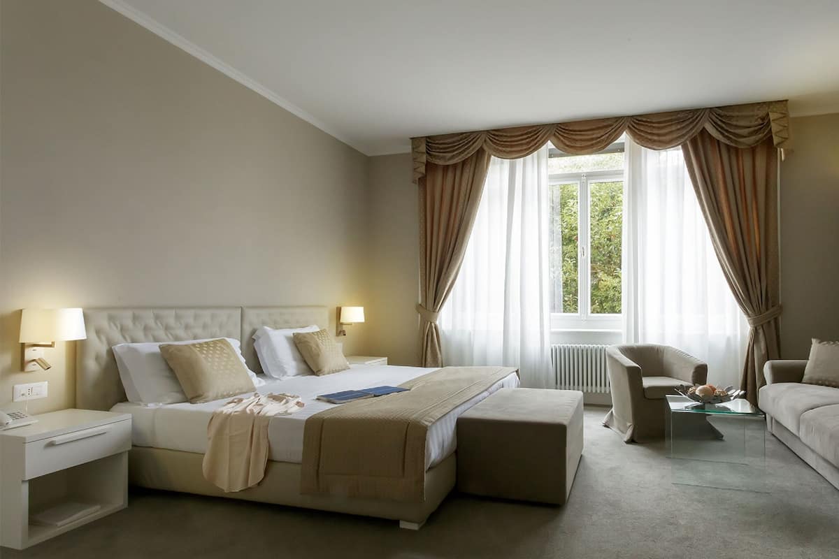 A hotel room with a bed, a sofa, a chair, a nightstand, and a lamp.