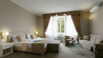 A hotel room with a bed, a sofa, a chair, a nightstand, and a lamp.
