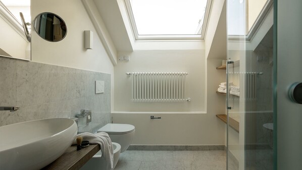 A modern bathroom with a skylight, a large sink, a toilet, and a glass shower enclosure. - Camin Hotel Luino (Luino)